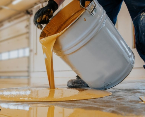 person pouring yellow liquid onto a floor - Innovative Garage Flooring polyaspartic floor coating